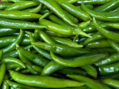 Bir pazarda büyük miktarda taze yeşil biber sergilenmektedir. Biberler canlı renklerini ve tazeliklerini gösterecek şekilde düzenlenmiş..