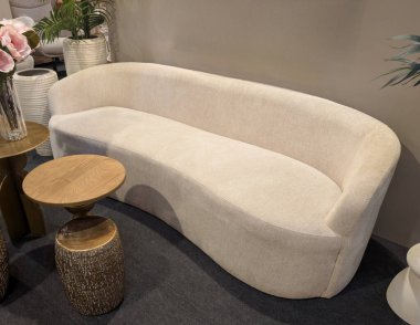 Modern bir mobilya mağazasında yumuşak kıvrımlı bir kanepe küçük yuvarlak bir masanın yanında yer alır. Ayarda nötr renkler ve basit tasarım unsurları yer alıyor.