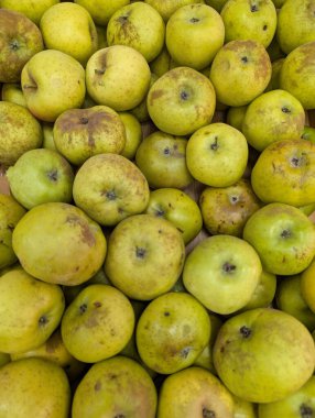 Bir market tezgahı büyük bir yeşil elma yığını gösteriyor. İnsanlar taze ürün aramak için etrafta dolanıyor. Hasat mevsimi müşteri çekerken sahne çok yoğun..