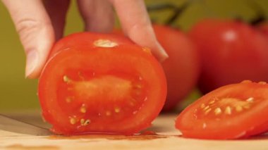 Kız kırmızı domatesleri dilimliyor. Yaklaş. Sarı arka plan. Makro kipi