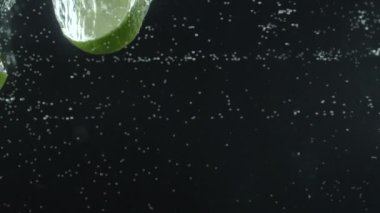 Limon dilimleri suya düşer. Siyah arka plan. Makro mod. Yavaş çekim