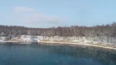 Karlı bir ormanda mavi bir gölün üzerinde uçmak. Kış. Karda mavi su olan göl