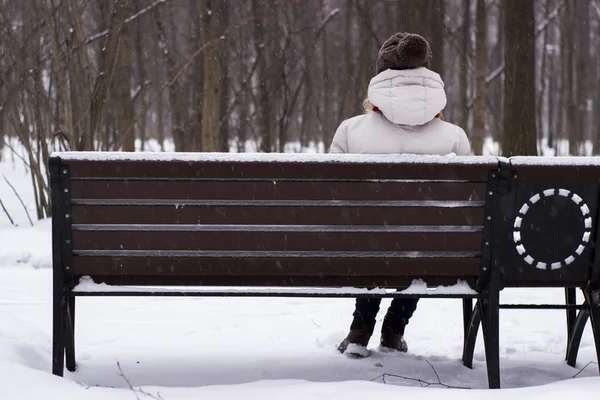 Joven hermosa chica sentada en el banquillo en el parque de invierno — Foto de Stock