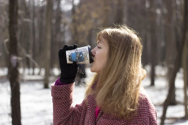 Hermosa mujer joven caminar al aire libre en el parque con una taza de café de plástico, que ella toma en sus manos — Foto de Stock