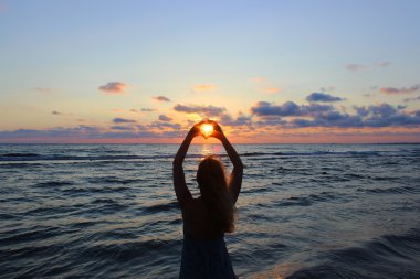 Siluet. Genç güzel kız ellerini üzerinden güneş ışınları yapmak kalp şeklinde geçti