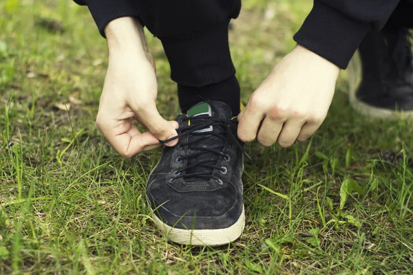 一个年轻人的手特写鞋带在运动鞋在绿草背景 — 图库照片