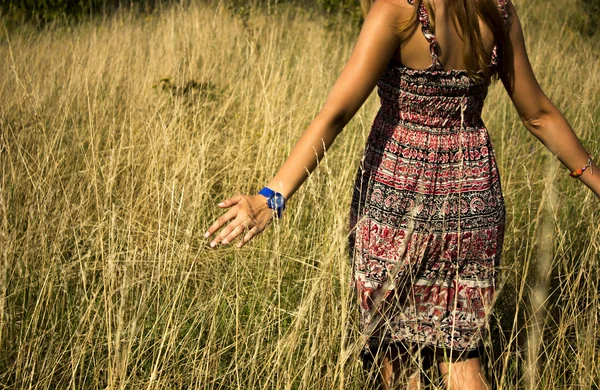 年轻漂亮的女孩在田里走和贯穿高乾草在夏季的一只手 — 图库照片