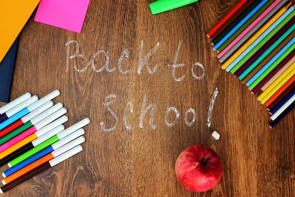 Colored pencils, felt-tip pens and markers, notebooks, stickers a red apple on the wooden background with the back to school inscription, top view.