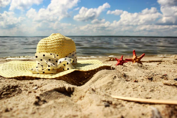 Strohhut und zwei rote Muscheln liegen im Sand und schließen den Hintergrund des Meeres — Stockfoto