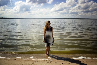 Genç güzel kız ayakta ve mavi denize yakın sarı kum tarafında bak