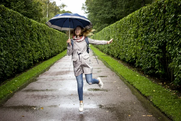 Mjuk och oskärpa befruktningen. Ung vacker flicka hoppning med blå paraply närbild nära de gröna gränderna från buskarna i regnet — Stockfoto