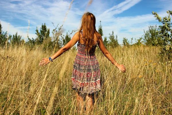 Young beautiful girl walking in the field and runs hand through the high dry grass at summertime — Stock Photo, Image