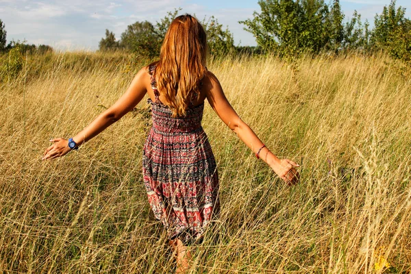 Jeune belle fille marchant dans le champ et court la main à travers l'herbe sèche haute en été . — Photo