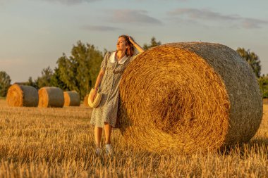 Mavi elbiseli genç kadın gün batımında samanlıklarla arka planda yakın çekim yapıyor..