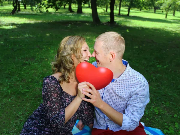 Jovem casal amoroso olhando um para o outro e segurando um coração vermelho. história de amor — Fotografia de Stock