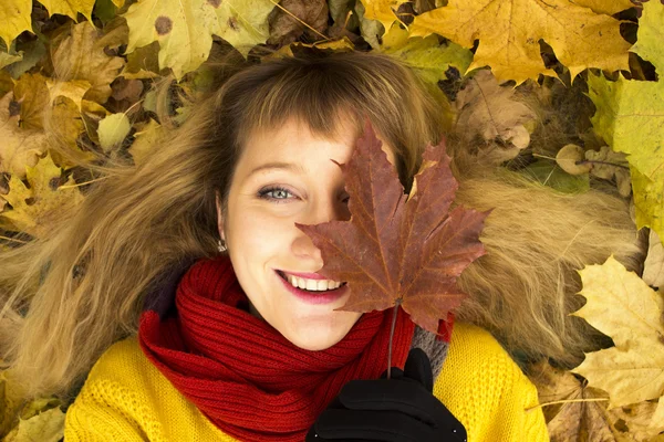 Jovem menina bonita deitada nas folhas de outono e sorrindo — Fotografia de Stock