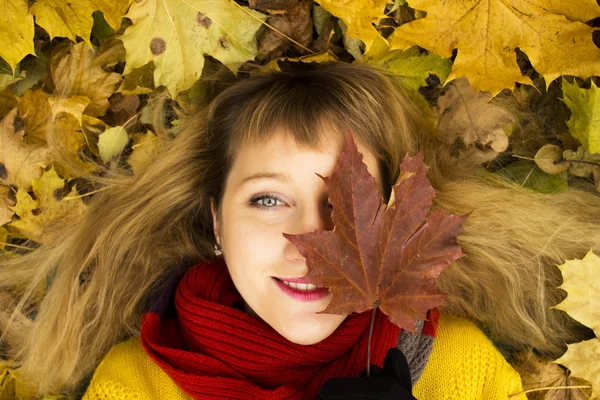 Young beautiful girl lying on autumn leaves and smiling — Stock Photo, Image