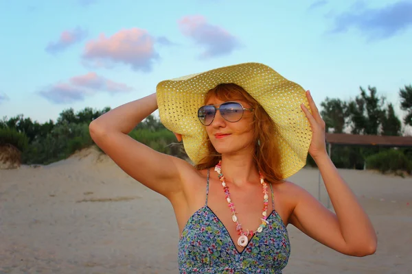 Giovane bella ragazza con un cappello in piedi sulla spiaggia la sera al tramonto — Foto Stock