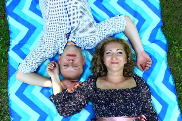 Jeune beau couple souriant et allongé sur la couverture sur l'herbe dans le parc — Photo