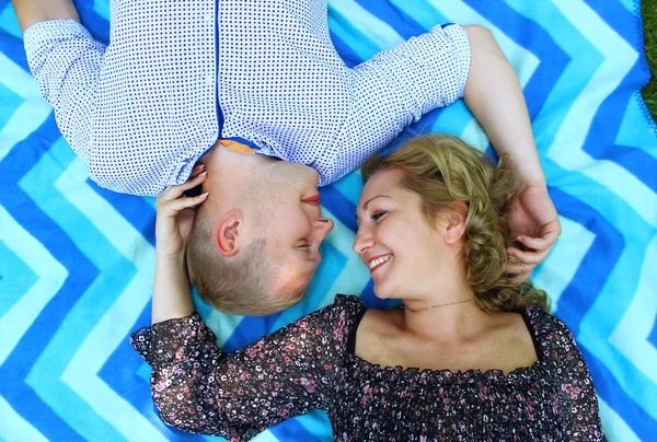 Jovem casal bonito sorrindo e deitado no cobertor na grama no parque — Fotografia de Stock