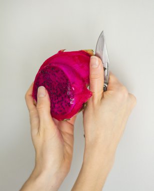 Gri dokulu arka plan üzerinde izole egzotik dragon meyve soyma. Parlak kırmızı mor Menekşe ciltlerinin meyve derili. Peeling işlemi içinde bıçak ile kadın el.