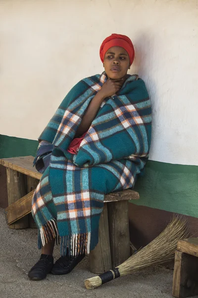Sudáfrica, Gauteng, Lesedi Cultural Village (centro único de la cultura africana) 04 de julio de 2015. Joven hermosa Sesotho mujer Bantu en tradicional hecho a mano colorido azul manta verde y sombrero naranja al lado de su casa . — Foto de Stock