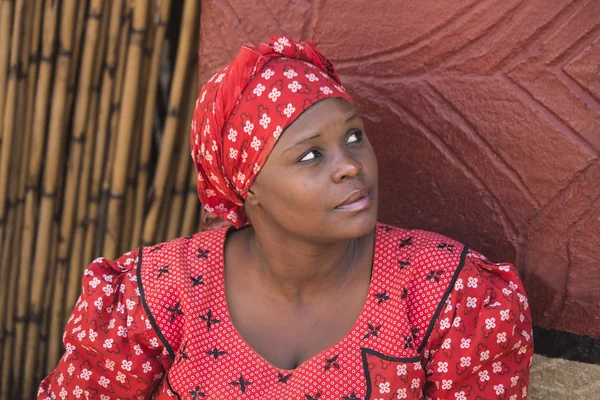South Africa, Gauteng, Lesedi Cultural Village (unique center of African culture) - 04 July, 2015 . Close-up portrait of Zulu woman Bantu in handmade red dress and african hat next to her house.