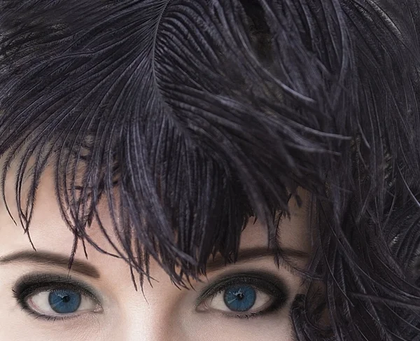 Gros plan portrait d'une mystérieuse jeune femme aux yeux bleu profond coiffée de plumes noires. Modèle de tir à la mode. Fumée maquillage des yeux. Une peau pure parfaite. Femme fatale. Style rétro. Style vintage . — Photo