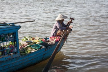 Kadın kürek teknesi ile çalışır, kaseler ve sebze ve meyve Kamboçya'daki Tonle Sap Gölü üzerinde yüklü sepetleri.