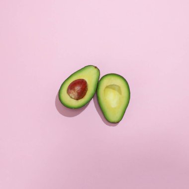 Meyve avokadosu pembe arka planda ikiye bölünmüş. Minimum düzlük.