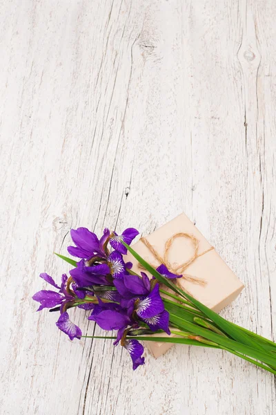 Buquê de íris flores e presente em um fundo de madeira leve . — Fotografia de Stock