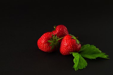 Yapraklarda siyah bir arka plan ile üç çilek.