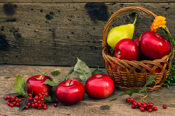 Pommes rouges et poire dans un panier sur un fond en bois — Photo