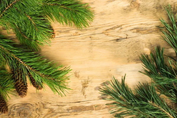 Wooden background with a frame of pine branches with cones — 图库照片