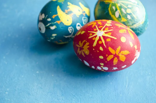 Tres coloridos huevos de Pascua hechos a mano aislados sobre un fondo azul — Foto de Stock
