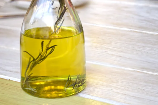 Bottle of olive oil and a sprig of rosemary inside. Transparent glass bottle on a wooden surface. — Stock Photo, Image