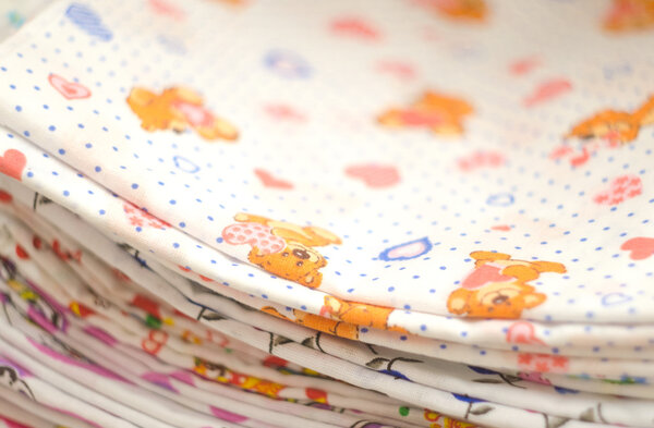 Baby swaddling with bears and hearts. Heap of folded linen of various colors. Pile of the washed and ironed linen.