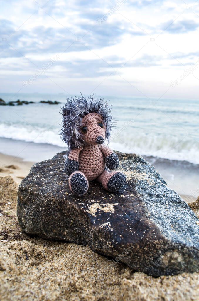 Knitted hedgehog by the sea. Crocheted toy vacation photo.