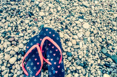 Deniz taşlarının arka planında kırmızı parmak arası terlikleri olan dişi otlar. Deniz bayramı fotoğrafı..