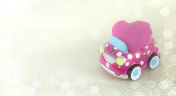 Un divertido coche de juguete para niños que lleva un cojín de corazón rosa. Concepto de celebración del día de San Valentín. Fondo de Bokeh — Foto de Stock