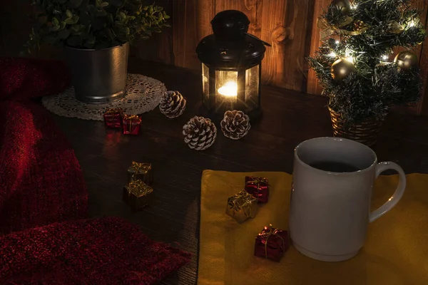 A cup of coffee on the table with a lit candle and the christmas tree