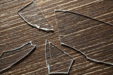 Eski ahşap bir masanın üzerinde kırık cam parçaları var.