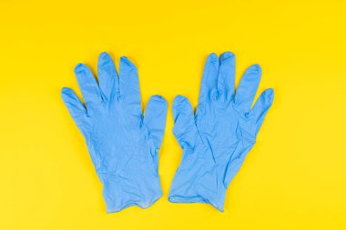 Sarı bir yüzeyde mavi lateks eldivenler.
