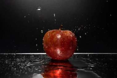 Düşen su damlalarıyla aynada dinlenen kırmızı bir elma.