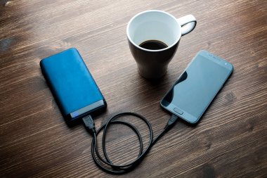 Tahta bir masada şarj olmak için güç bankasına bağlı bir cep telefonu.