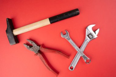 Bir çekiç, bir çift kerpeten ve kırmızı bir yüzey üzerinde anahtarlar.