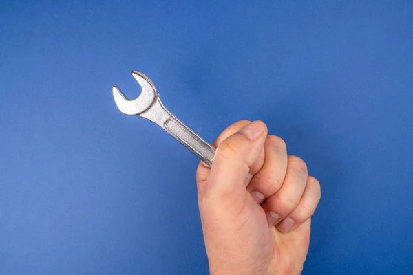 A wrench in the hand in front of a blue background