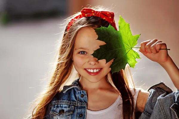 Güzel gülüşü ve elinde akçaağaç yaprağı olan tatlı bir kız.