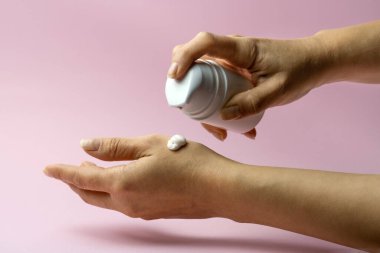 Kadın elini pembe arka plan fotokopi alanındaki kozmetik krem losyonuyla nemlendiriyor.