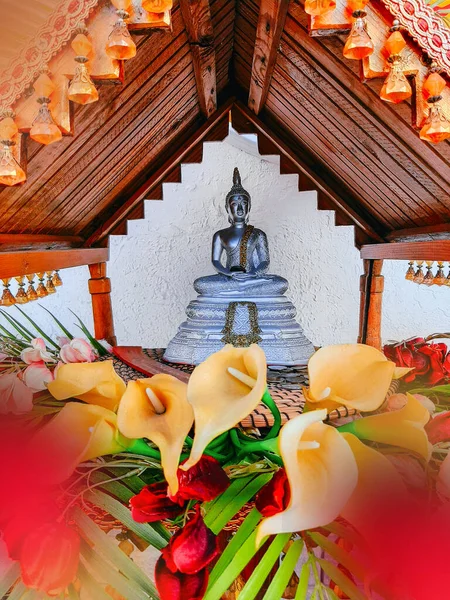 a small altar with a metal statue of Buddha and flowers offerings